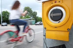 A woman on a bicycle rides past crossing signal button