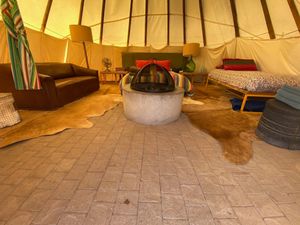 The inside of a tipi with two beds, a fire pit, and a love seat