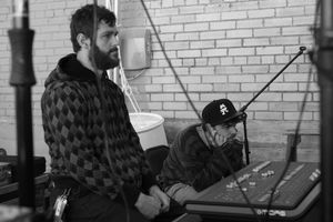 Two expressionless soundboard Engineers watch the band play (out of frame)